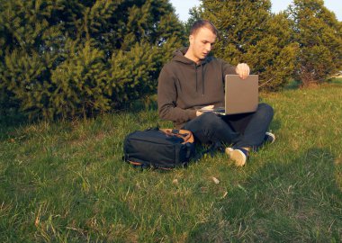 Genç adam laptopta çalışıyor çimlerin üzerinde oturuyor.