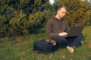 Genç adam laptopta çalışıyor çimlerin üzerinde oturuyor.