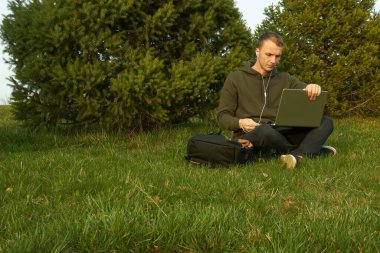 Genç adam laptopta çalışıyor çimlerin üzerinde oturuyor.
