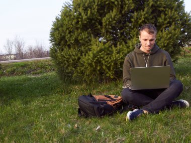 Genç adam laptopta çalışıyor çimlerin üzerinde oturuyor.