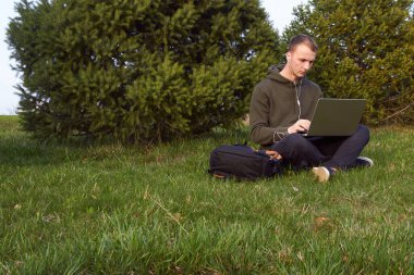 Genç adam laptopta çalışıyor çimlerin üzerinde oturuyor.