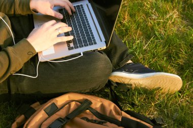 Genç adam laptopta çalışıyor çimlerin üzerinde oturuyor.