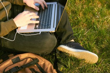 Genç adam laptopta çalışıyor çimlerin üzerinde oturuyor.