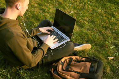 Genç adam laptopta çalışıyor çimlerin üzerinde oturuyor.