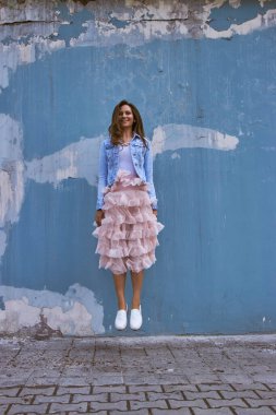 Pembe etekli kız mavi duvarın arkasında zıplıyor.