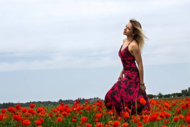 Güzel, genç sarışın kız, afyon tarlalarının arasında güzel bir elbise içinde..