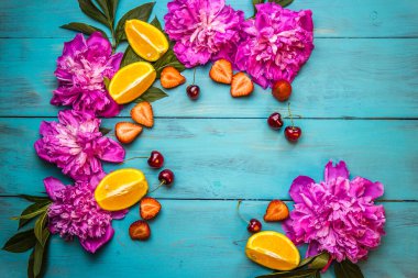 Tahta bir turkuaz arka planda pembe şakayık çiçekleri ve dilimlenmiş meyve uzanır.