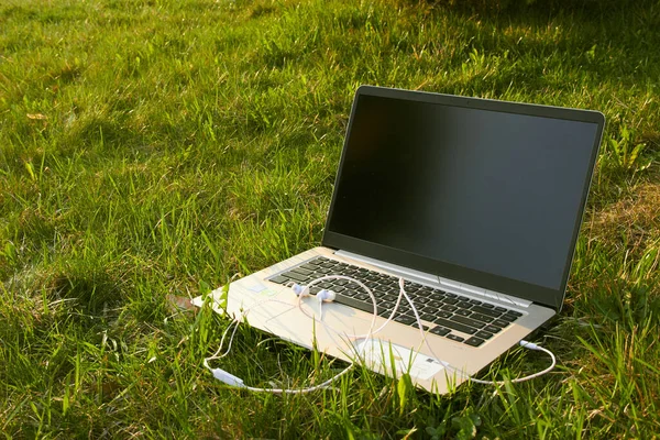 laptop with headphones stands on green grass