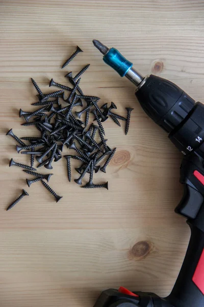 İnşaat aletleri tornavida ve vidalar ahşap bir masanın üzerinde yatıyor.