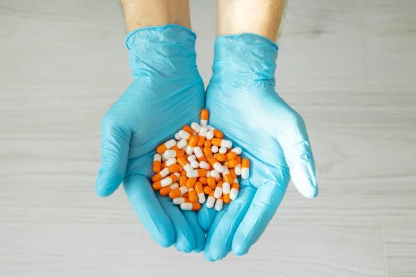 male hand in a medical glove holds a handful of orange pills