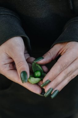 Yeşil manikürlü kız elinde yeşil bir kızılcık tutuyor.