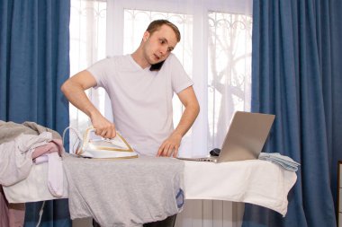 Evde kendini izole eden genç bir adam uzaktan çalışıyor ve ütü yapıyor..