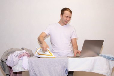 Evde kendini izole eden genç bir adam uzaktan çalışıyor ve ütü yapıyor..