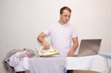 Evde kendini izole eden genç bir adam uzaktan çalışıyor ve ütü yapıyor..