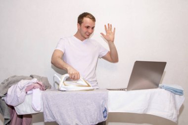 Evde kendini izole eden genç bir adam uzaktan çalışıyor ve ütü yapıyor..