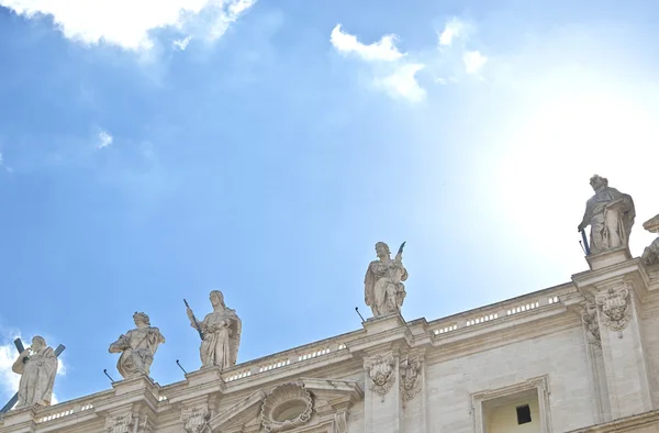 Beelden op het dak van St. Peter's Basiliek. Boven het hoofd van een van de sculpturen zon schijnt en herinnert halo. — Stockfoto