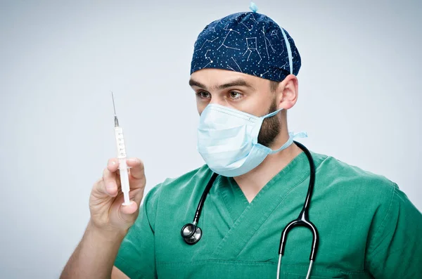 Male doctor in green scrubs, mask and hat holding a syringe with medicine. — Stock Photo, Image