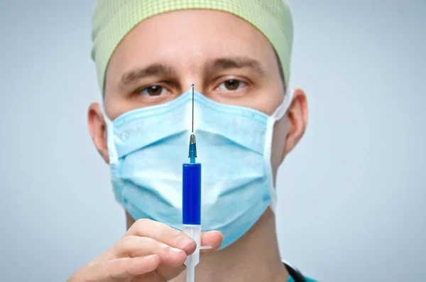 O médico com uma tampa verde e máscara segurando uma seringa com medicamento . — Fotografia de Stock