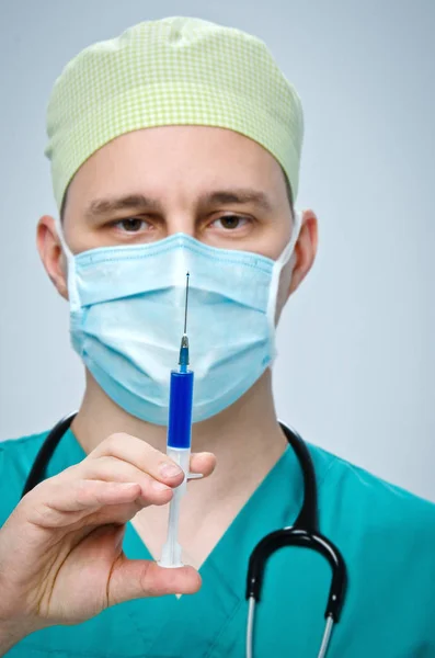 El médico con un sombrero verde y una máscara azul sosteniendo una jeringa con medicamento . —  Fotos de Stock