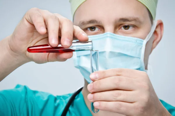 緑の帽子と青いマスクの医師別のガラス管に 1 つのテスト チューブから赤い液体を注ぐ. — ストック写真