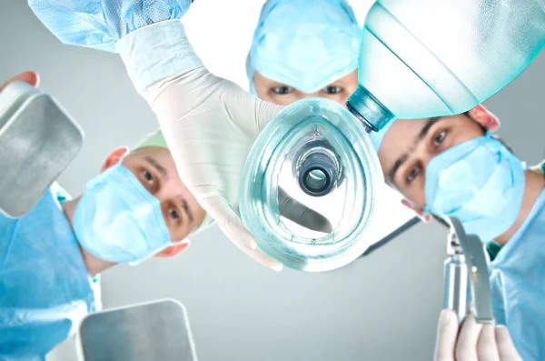 Uma equipa de três médicos na sala de operações. Mulher médica segurando uma máscara respiratória, um homem médico segurando uma lâmina para intubação e outro homem médico segurando um desfibrilador . — Fotografia de Stock