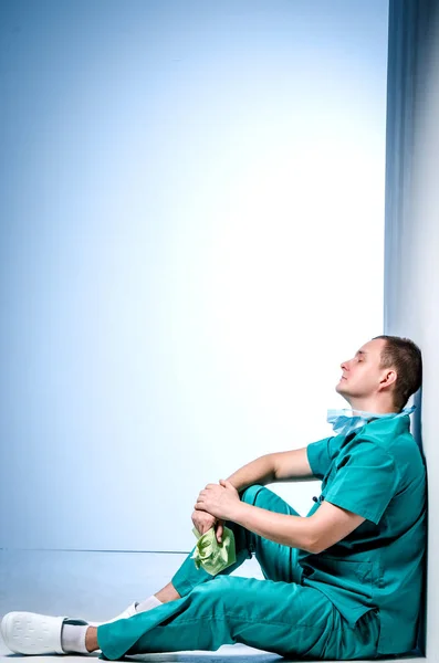 Καταπονημένος γιατρός κάθεται μετά από χειρουργική επέμβαση σε ένα διάδρομο νοσοκομείο. — Φωτογραφία Αρχείου