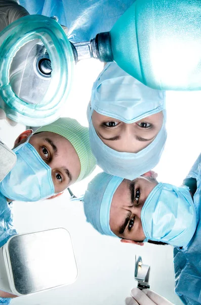 Τρεις γιατροί έσκυψε ο ασθενής στο χειρουργείο. Κρατάνε μια μάσκα οξυγόνου, απινιδωτής και λεπίδα για διασωλήνωση. — Φωτογραφία Αρχείου