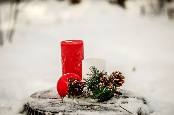 Três velas decorativas e um ramo de pinho com uma pinça em um toco de árvore na floresta de inverno . — Fotografia de Stock