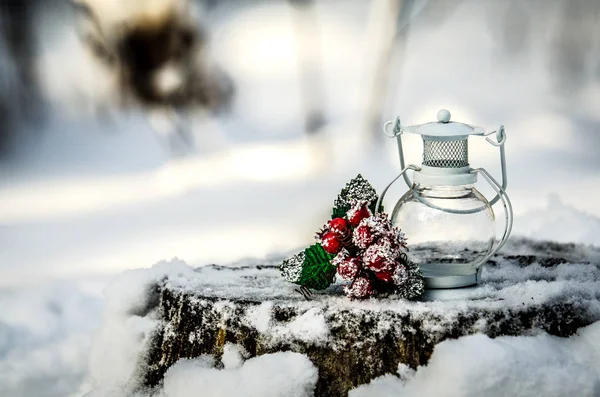 A lâmpada branca e um ramo com bagas vermelhas e folhas verdes em um toco de árvore coberto de neve . — Fotografia de Stock