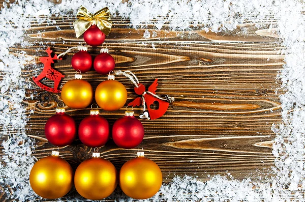 Christmas tree, lined with red and gold Christmas tree balls. Christmas tree toys lie on a wooden surface. Next to the tree is a red wooden toy in the form of a deer and an angel.