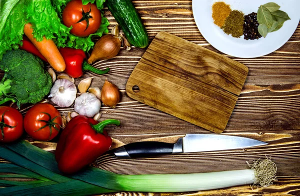 Kırmızı ve yeşil sebze ve yeşillik bir ahşap yüzeye yalan. Sebze yanındaki küçük ahşap plaka ve bıçak olduğunu.