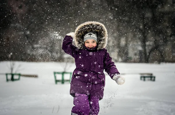 Ragazzina in tuta da sci che gioca a palle di neve. Sta per lanciare una palla di neve. La ragazza sta sorridendo ed è molto divertente . — Foto Stock