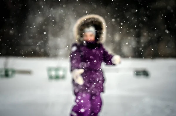 Silhueta turva de uma criança brincando na neve. Em primeiro plano está uma grande mosca branca de flocos de neve . — Fotografia de Stock