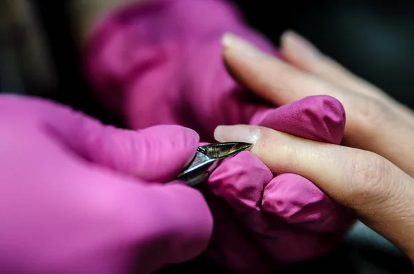 El proceso de eliminación de las cutículas con pinzas para la manicura. Manos Mago guantes de látex reservados . —  Fotos de Stock