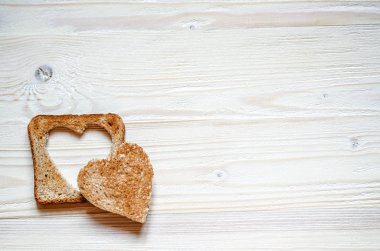 Beyaz ahşap yüzeyde eksizyon ile tost kalbinde yer almaktadır. Kızarmış ekmek üzerine bir tahıl kalp ise.