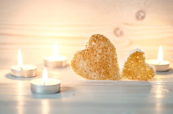 Dois croutons de pão na forma de corações estão entre as velas decorativas. Sua luz suave de velas ilumina . — Fotografia de Stock