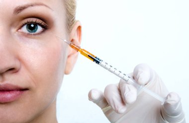 Doktor hastaya göz çevresi cilt gençleştirici bir enjeksiyon yapıyor.