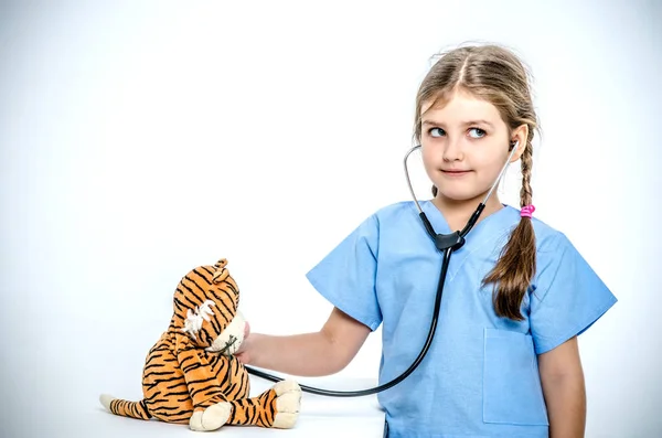 Маленькая девочка в хирургическом костюме слушает своего игрушечного тигра с помощью фонендоскопа . — стоковое фото