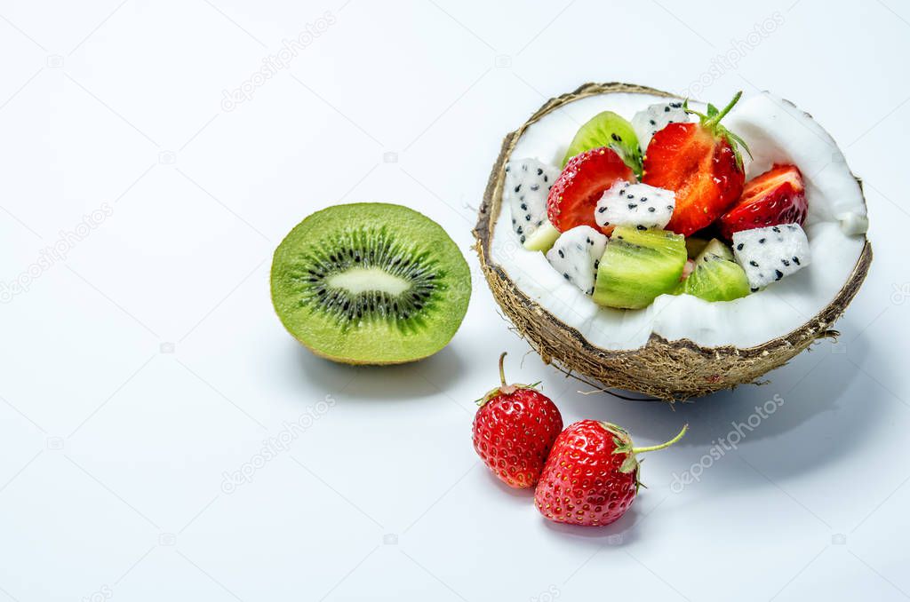 Pieces of strawberries, kiwi and dragon fruit in a half of coconut. Nearby lie two berries of strawberries and half kiwi.