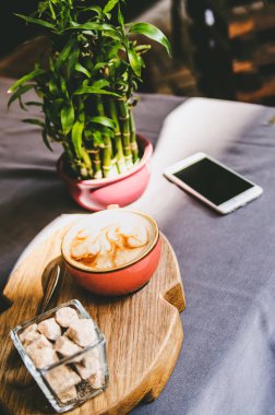 Telefon, kapuçino, kahverengi şeker ve bir vazo bambu ile masaya standı.