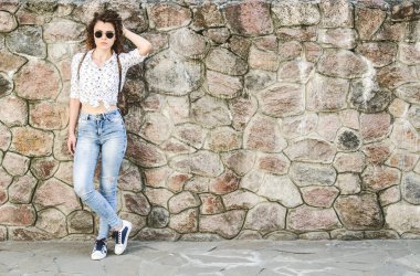 Kot pantolon ve beyaz gömlek bir kıvırcık kız saçını ayarlama taş duvar tarafından duruyor.