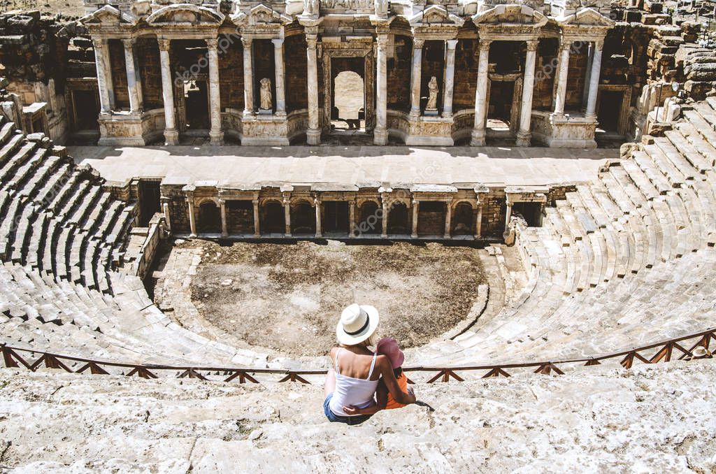 Mom and daughter are sitting on the steps of an ancient amphitheater, located in Hierapolis, Pamukkale, Denizli province, Turkey.