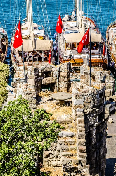 The tower of the castle of St. Peter in Bodrum. Among the tower is a round stone table, and in the background are visible yachts standing in the bay.