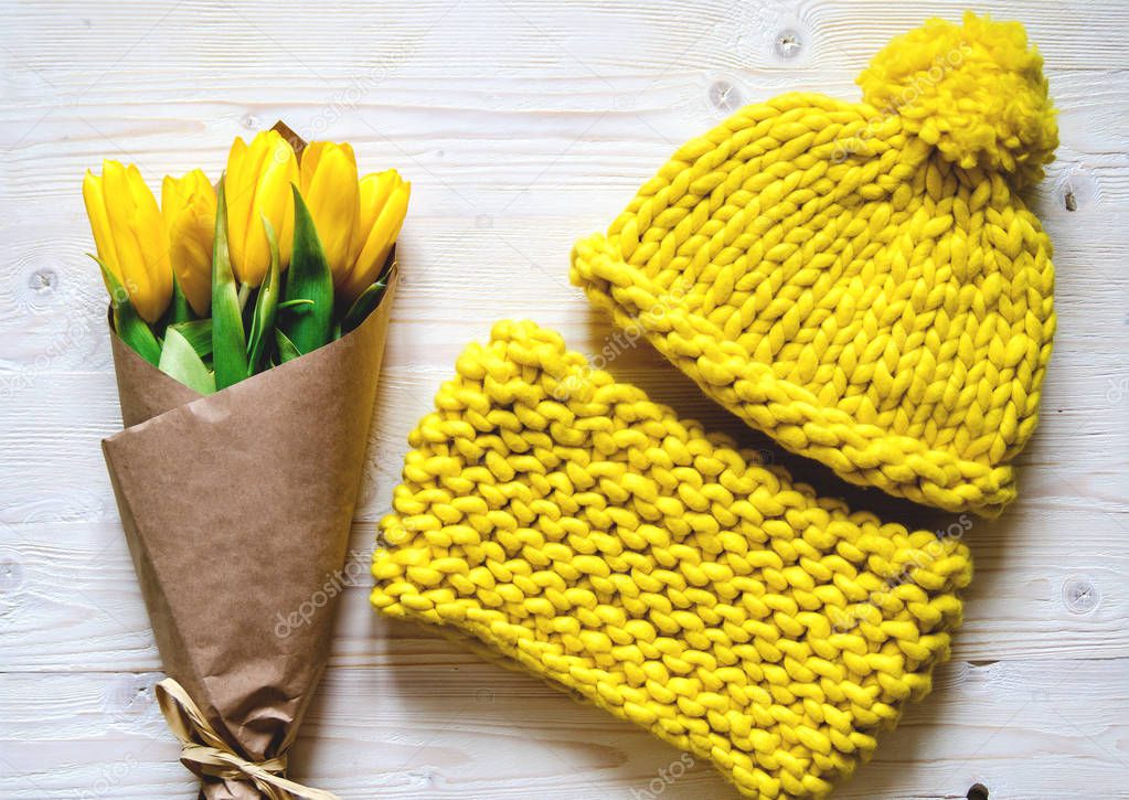 A yellow knitted hat and a snore from thick Merino yarn. Nearby is a bouquet of yellow tulips.