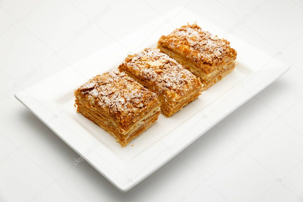 French Napoleon Cake of puff pastry with sour cream on a white plate close-up. Nutritious dessert. Selected Focus