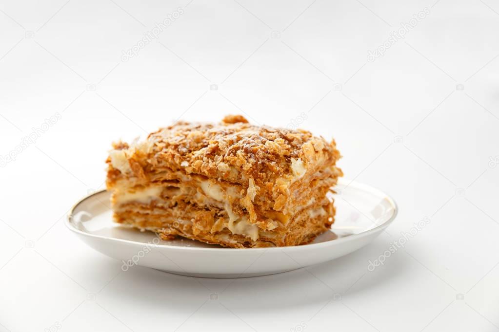 French Napoleon Cake of puff pastry with sour cream on a white plate close-up. Nutritious dessert. Selected Focus