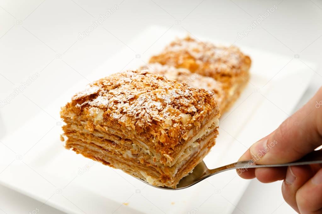 French Napoleon Cake of puff pastry with sour cream on a white plate close-up. Nutritious dessert. Selected Focus
