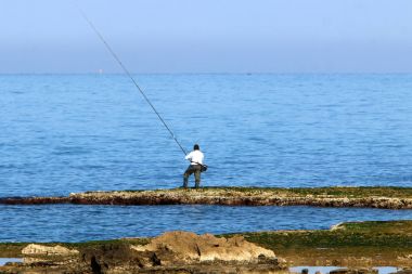 balıkçı kıyıda oturur ve balık yakalar 