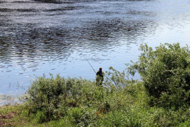 balıkçı kıyıda oturur ve balık yakalar 