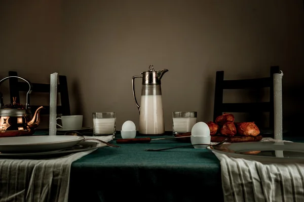 Stilleven. rustieke diner. kruik, kaarsen, thee, eieren, melk broodjes op tafel — Stockfoto